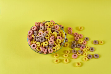 breakfast cereal rings on a yellow background in a plate and scattered nearby