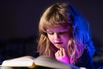 Cute little boy reading book. Child with open book. Homeschool lesson. Concentrated little boy on bed reading book at home. Development of the child. Clever child boy.