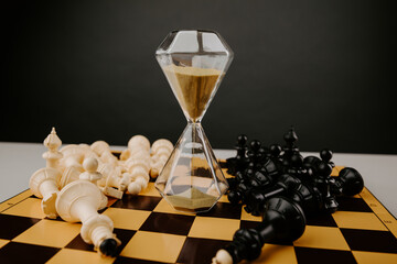 Hourglass on a chessboard with a bunch of chess pieces close-up