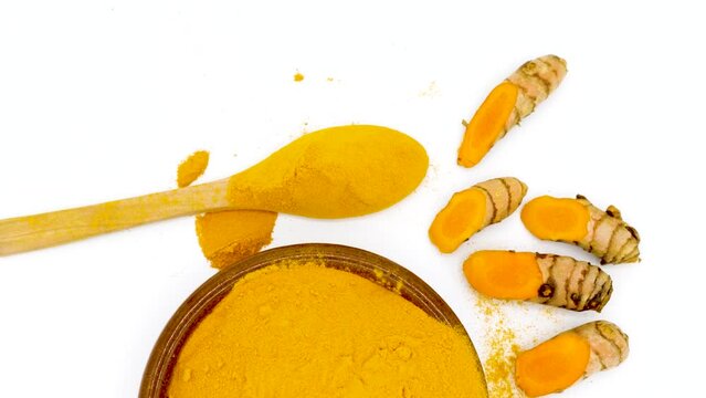 Turmeric powder in a circular shape next to fresh cut turmeric on white background