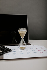 Hourglass on a desktop with calendar and laptop, year change or deadline concept, vertical image
