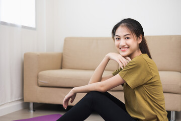 Young beautiful asian woman sitting pose smiling to camera. Cheerfully sporty female workout and exercise wearing sport wear at home. Charming woman fitness training and stretching on yoga mat.