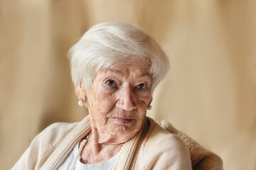Portrait of a confident, elderly woman after 85 with gray hair in a light beige cardigan