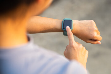 Woman checking sports smart watch in the city at sunrise. Asian female adjusting smart watch before workout outdoor. Exercise in the morning. Healthy and technology lifestyle concept.