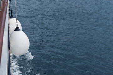 Buoy hangs from sailing ship and foam on sea surface