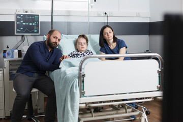 Parents and sick little girl watching television comedy program while sitting in pediatric clinic...