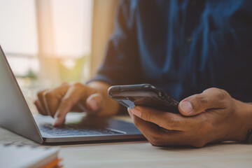 Close up of man hands with mobile phone, Businessman hand using laptop and smart phone working at home office.