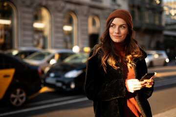 Beautiful smiling woman with mobile phone walking on the street. Happy woman typing a message.