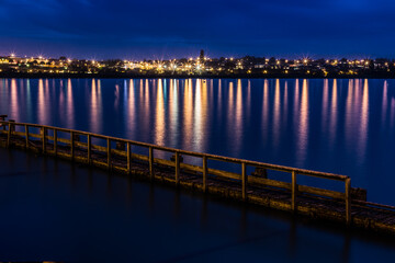 Fototapeta premium Long Exposure at Night, Twilight Across Water, Looking at City Lights with View of Pier in Foreground. In Timaru, New Zealand