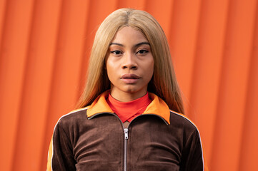 Joven mujer afroamericana con cabello largo rubio y ropa deportiva sobre un fondo de color naranja