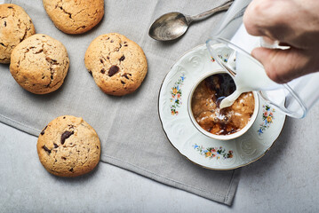Hand pouring milk into espresso coffee cup with chocolate bisquits on table. Afternoon coffee brake with chocolate cookies.