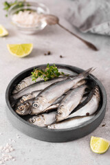 fresh large sprats with lemon, herbs and sea salt on a gray plate, close-up