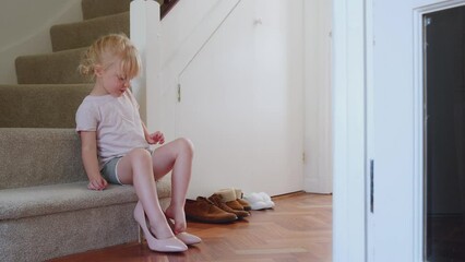 Young girl sitting on stairs dressing up and putting on Mother's high heeled shoes - shot in slow motion