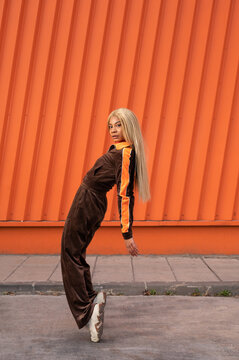Una alegre mujer afroamericana con ropa deportiva bailando en la calle sobre un fondo naranja