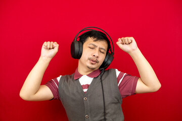 An Asian man is having fun and dancing while listening to a song using a headset. red background.