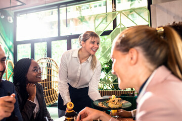 Smiling waitress serving meal to group of business people in restaurant.