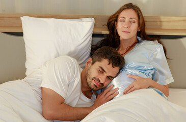 Delighted father tenderly lie down on belly of beloved pregnant wife on bed to feel and hear unborn baby kicking in stomach