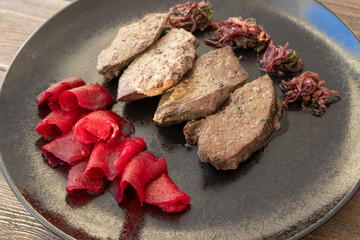 Beef liver cooked in the oven with red onion on a dark plate.
