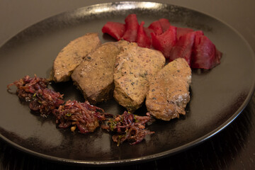 Beef liver cooked in the oven with red onion on a dark plate.