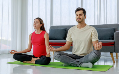 Healthy couple calmly relax and quietly sit on yoga floor mat for morning meditation and mindfulness contemplation as maternity and pregnancy exercise for wellness of belly and unborn baby.