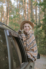 Young blonde woman looking at the forest from her car. Road trip.