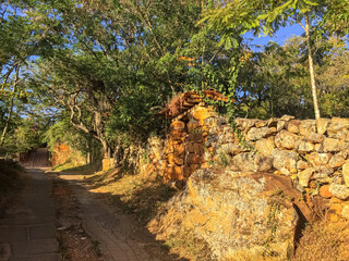 Old stone wall with entrance gate and lush green in the late afternoon light, Barichara, Colombia