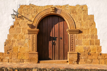 Fototapeta premium Old door framed with stone artwork and wall at a historical house, Barichara, Colombia