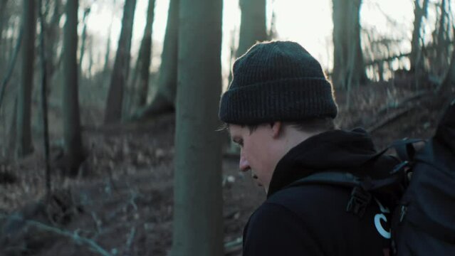 Young male adventurer walking through a forest with a beanie on carrying his backpack. Sunset 4K Outdoors Adventure Slow Motion Anamorphic