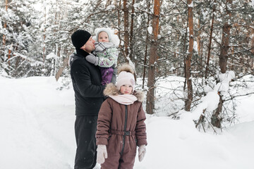 Fototapeta na wymiar father with two daughters walking through the winter forest
