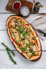 A long pizza with arugula and seafood on a wooden white background. Pizza with shrimp, squid and mussels.