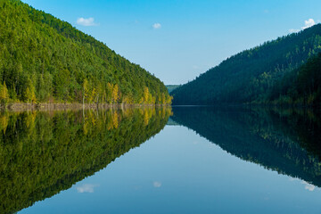 forest and mountain are reflected in the river summer sunny day