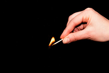 A woman's hand holds a lit match on a black background. A symbol of home comfort and keeping the hearth.