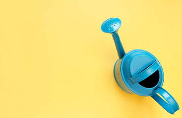 blue watering can on yellow background. Creative concept of investment, growth, success in business and life or hello summer. Top view Flat lay