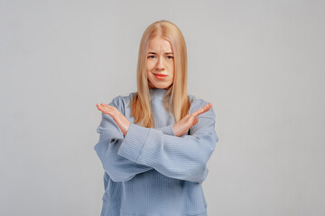 Young blonde woman showing stop gesture with crossed hands. Serious teen girl refusing something...