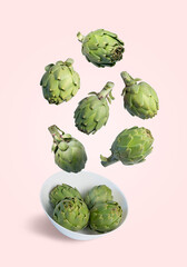 Flying fresh artichokes falling into a bowl isolated from the background 