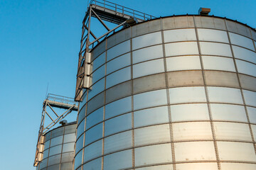 A large modern plant near a wheat field for the storage and processing of grain crops. view of the silver silos illuminated by the light of the setting sun against the blue sky. harvest season