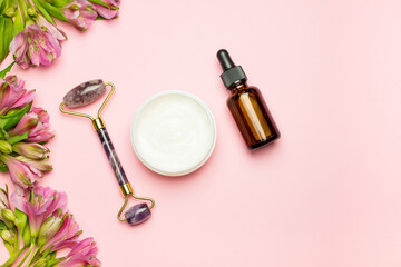 Obraz na płótnie Canvas Face roller with cosmetic serum, face cream on a pink background and rose petals. Skincare, natural organic cosmetics concept. Top view, flat lay.