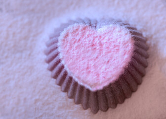 Heart-shaped silicone shape sprinkled with pink powdered sugar on white background