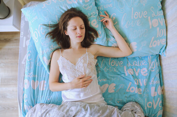 Young happy woman lies, sleeping in bed in a nightgown, pajamas in a cozy bedroom in home