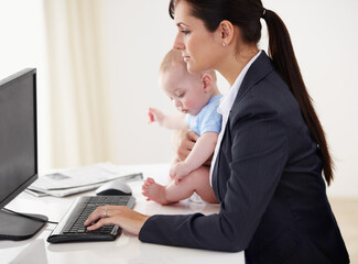 Mommys got a job to do.... Young working mother holding a baby while working on her computer.