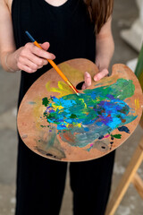 Painter artist stands in studio holding brush and palette with mixed paints in hands