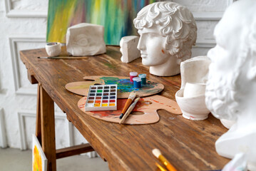 Painter workplace with aquarelle palette, paintbrushes and apollo head model on the desk