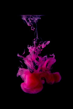Purple-red acrylic ink is scattered in the water creating strange shapes on a black background. abstract background