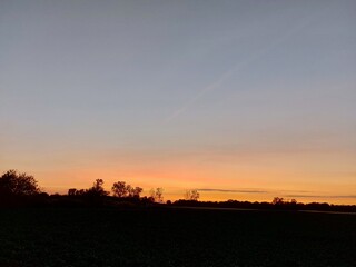 D&auml;mmerung auf einer Agrarlandschaft. Der Himmel wird dunkel. Die Sonnenunterg&auml;nge im Westen mit R&ouml;tung. Der Mond erscheint am Himmel &uuml;ber der Wiese. Der Wald verwandelt sich in Silhouetten. Abend.