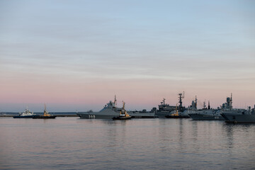 Fototapeta na wymiar Two naval harbor tugs against the background of warships in the Petrovskaya pier of Kronstadt. Evening sunset. Russia, Kronstadt, July 26, 2020