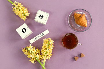 Calendar for March 8: cubes with numbers 0 and 8, the name of the month of March in English, yellow hyacinths, a cup of tea, homemade cakes on a pastel background, top view