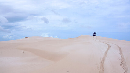 Fototapeta na wymiar A all-terrain vehicle as public transportation is driving offroad on a big dune with car tracks in the sand in the Lencois Maranhenses in Brazil