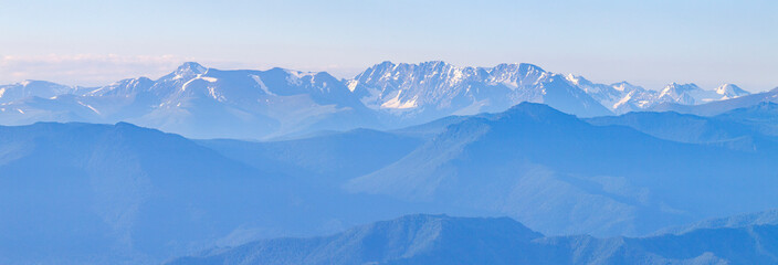 Fototapeta premium Mountains in blue haze, panoramic view. Peaks in the clouds, valley and mountainsides.