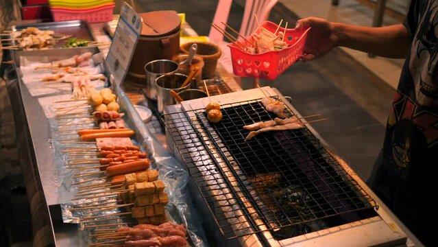 Local Asian Street food: Chef Cooking Traditional Thai Satay on Grill at Night Food Market. Phuket Town, Thailand. 4K High Quality Footage Video.