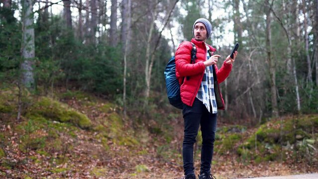 Young solo backpacking trekker adventurer traveller following the indication from a map in his new modern smartphone device connected to 5g wireless in remote natural countryside forest